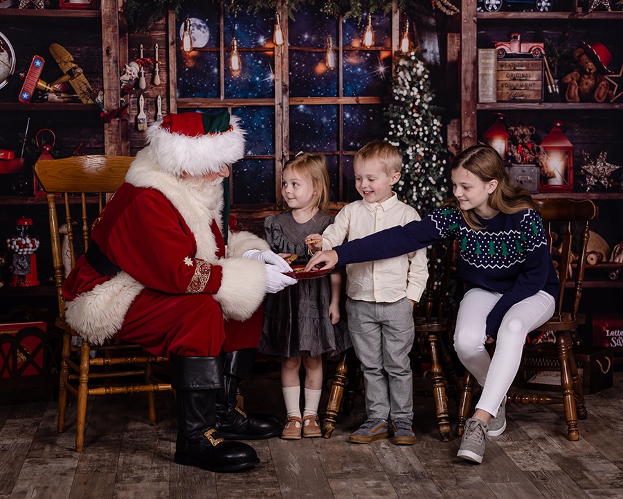 three siblings eating cookies with santa